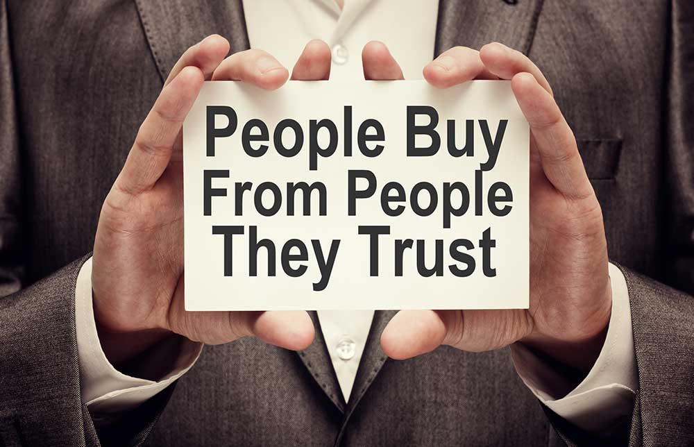 A businessman holding a card with a message that says, “People buy from people they trust.”