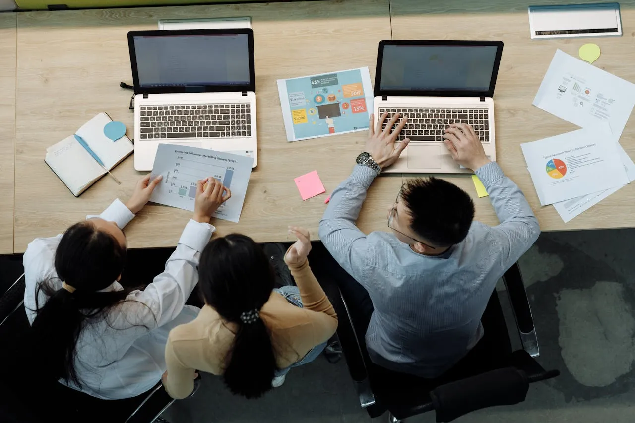 Digital marketing agency experts collaborate at a workspace with laptops, papers, and colorful sticky notes. 