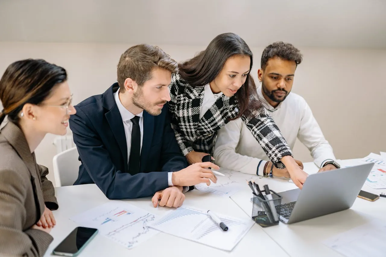 A team gathered around a laptop and data charts, collaborating to identify gaps and opportunities in their digital marketing strategy.