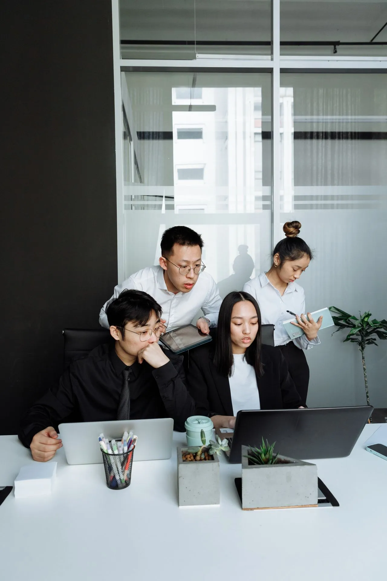 A focused office scene with three corporate website designers gathered around laptops at a white table. 