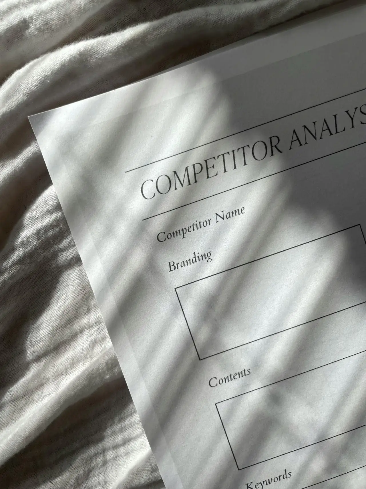 A competitor analysis sheet lies on textured fabric. 