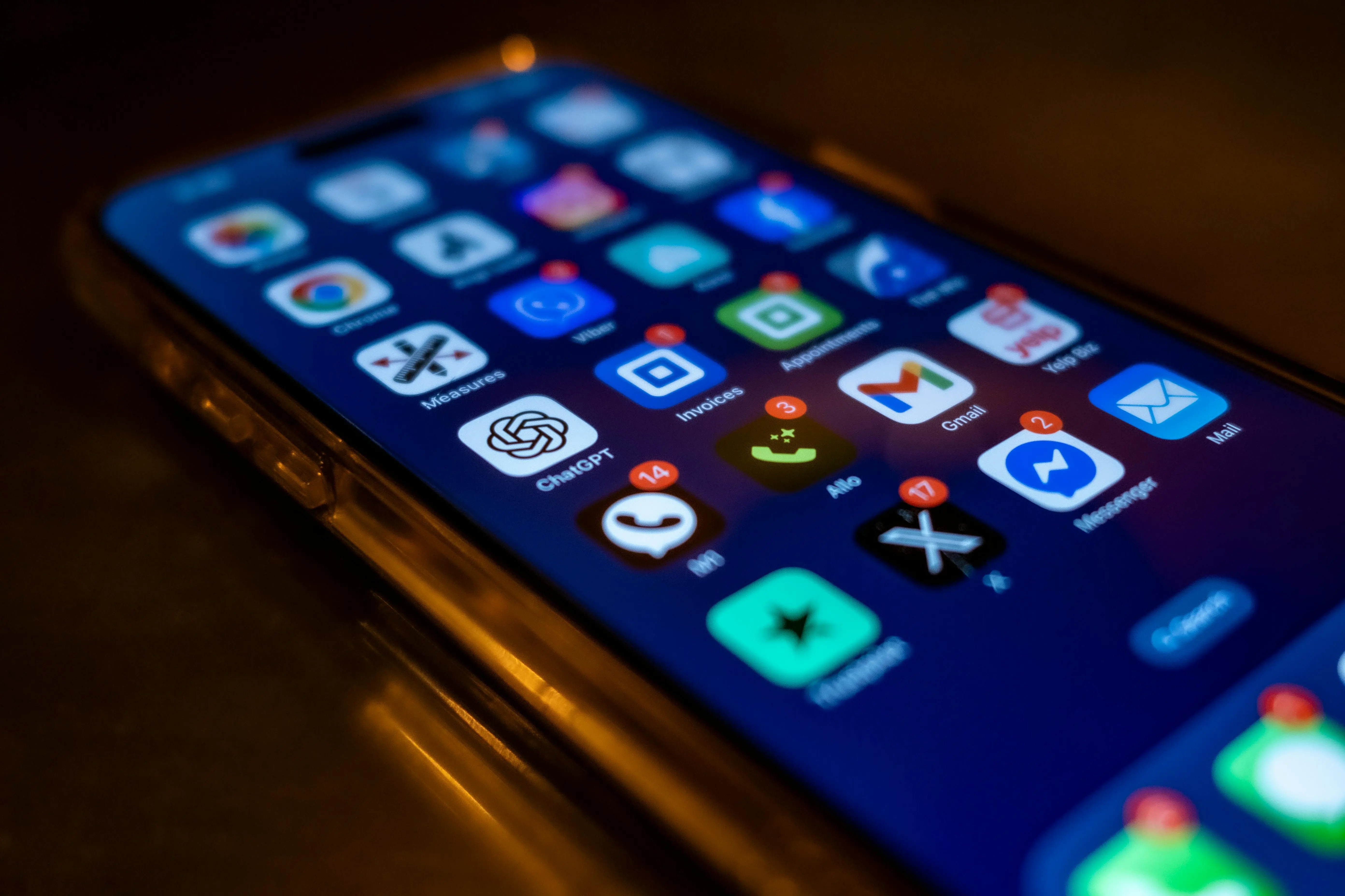 Close-up of a smartphone screen displaying various app icons with notification badges. The screen is dark, creating a focused, digital atmosphere.