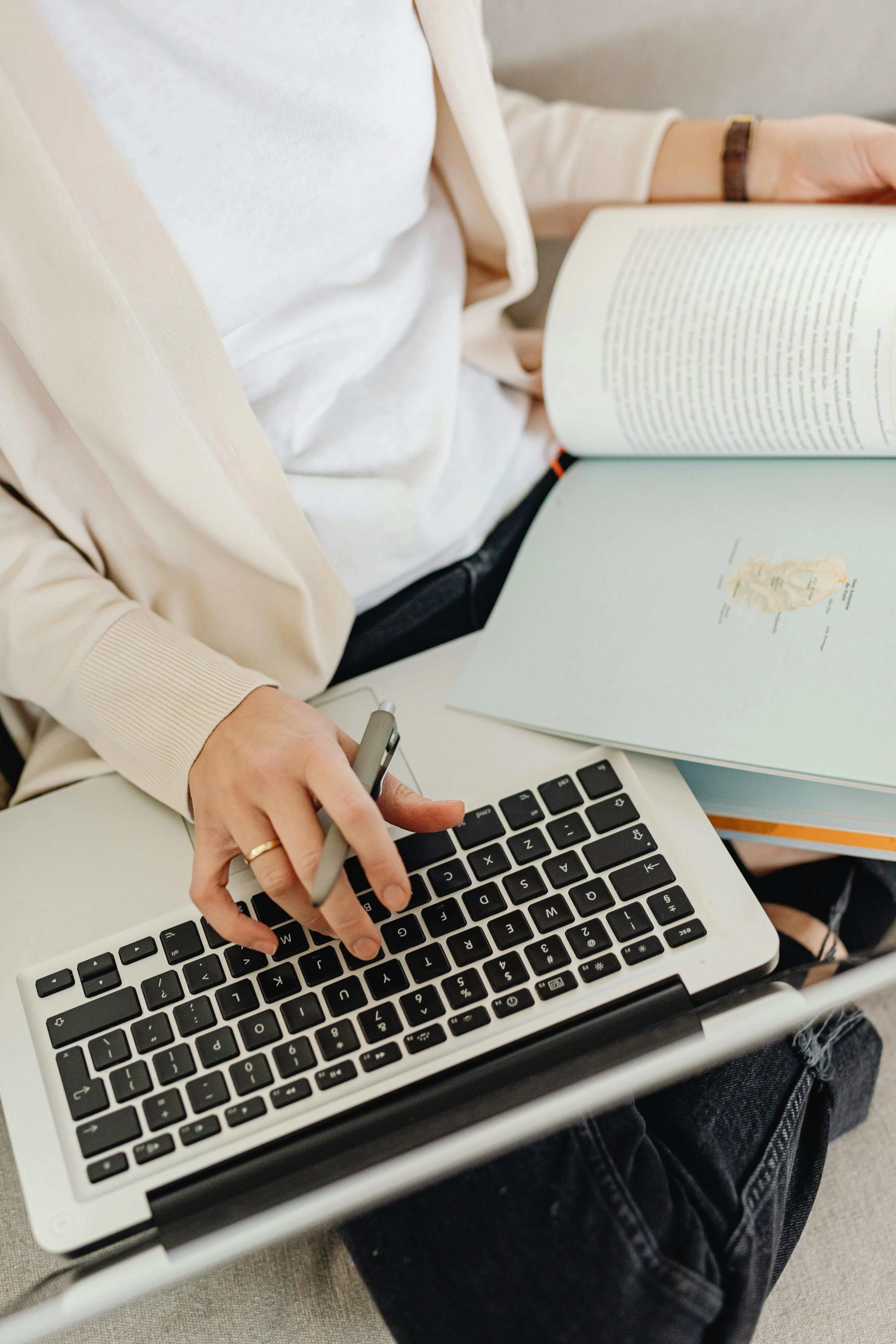 Person works on content strategy on a laptop, holding a pen and an open book on their lap. 